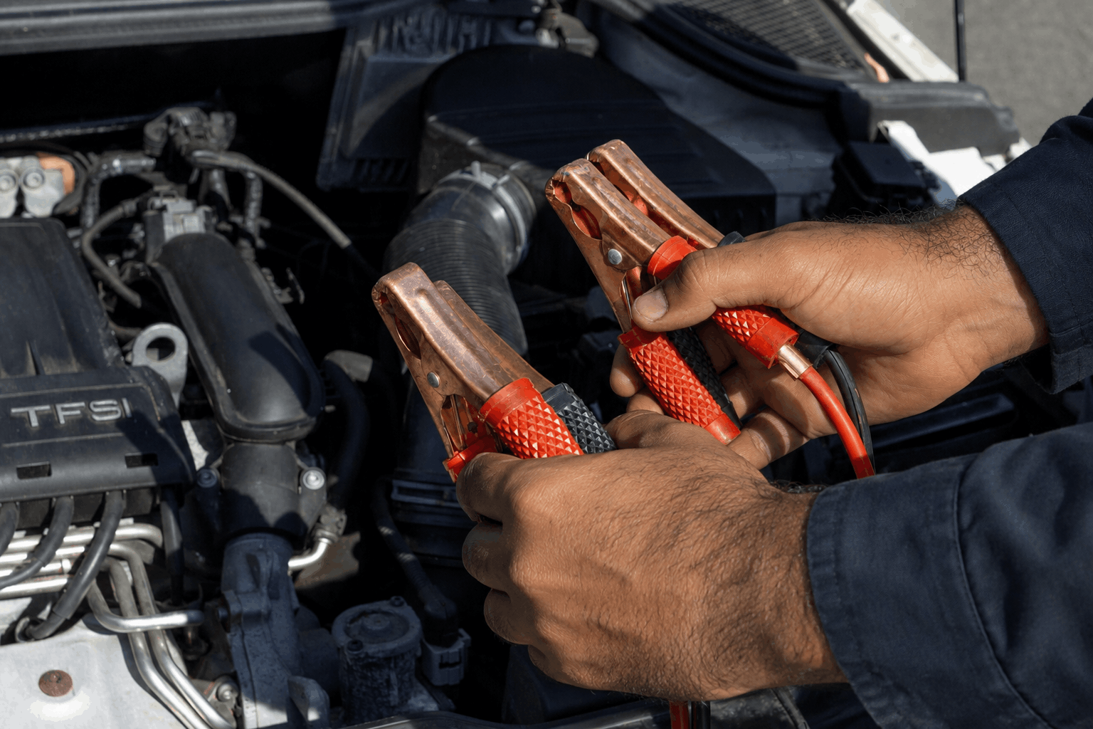 JumpStart.ae technician connecting a booster pack to a car battery, Dubai skyline behind